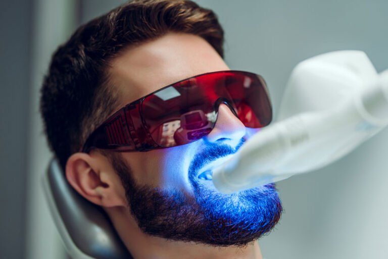 Teeth whitening patient with the blue light on his mouth and red glasses to reduce the brightness of the light