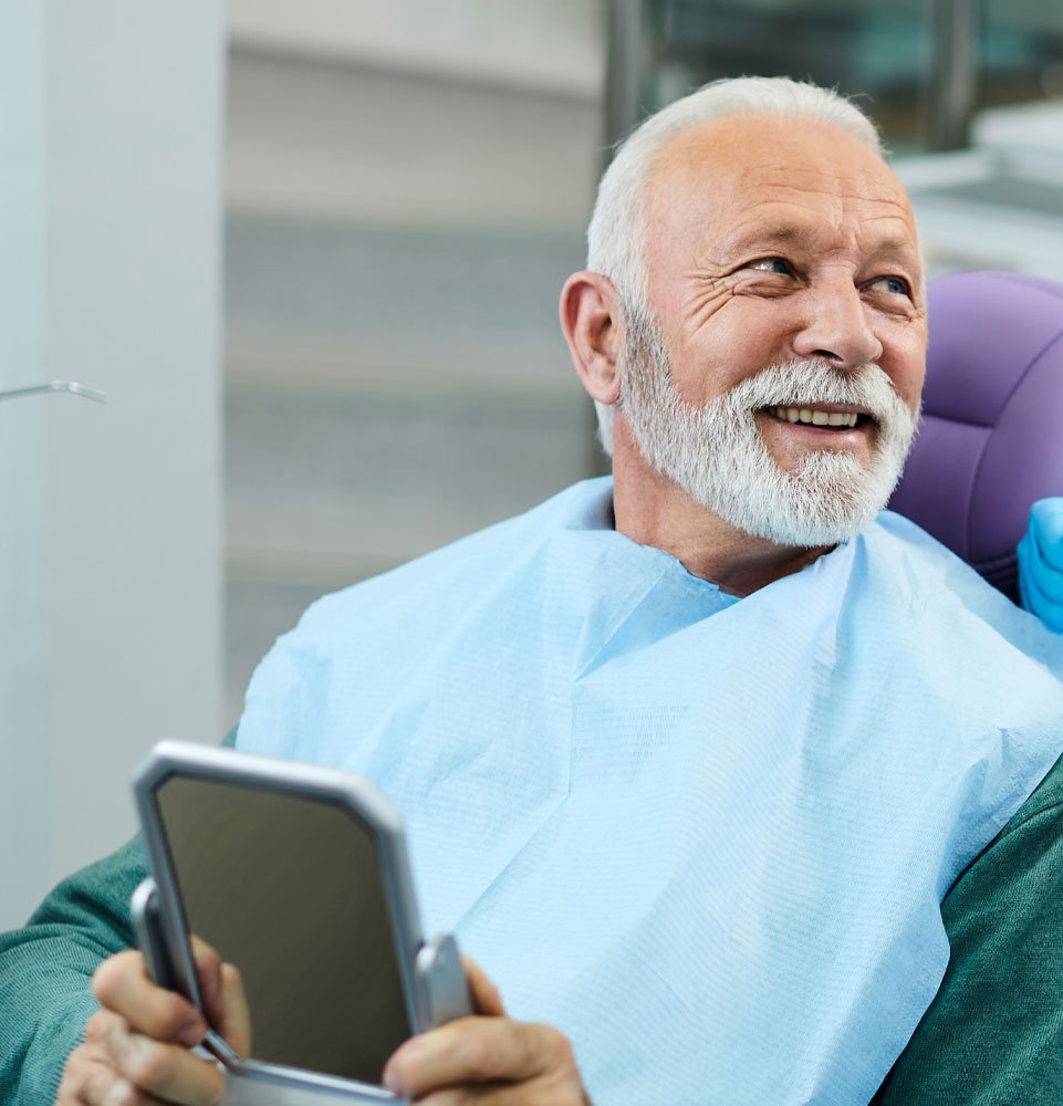 older man with new smile happyl ooking in mirror